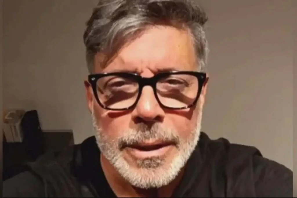 Alexandre Frota aparece sério em foto de close, usando óculos e camisa preta.