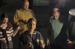 Aline Barros em momento de oração ao ar livre durante a noite, com algumas pessoas de olhos fechados e mãos erguidas.