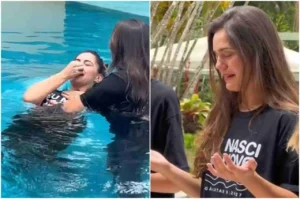 Atriz sendo batizada por imersão em piscina, emocionada, vestindo camiseta com frase bíblica, durante cerimônia evangélica ao ar livre.