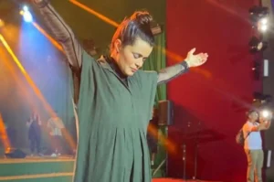 Cantora Damares de olhos fechados e braços abertos durante ministração no palco, sob luzes de show.