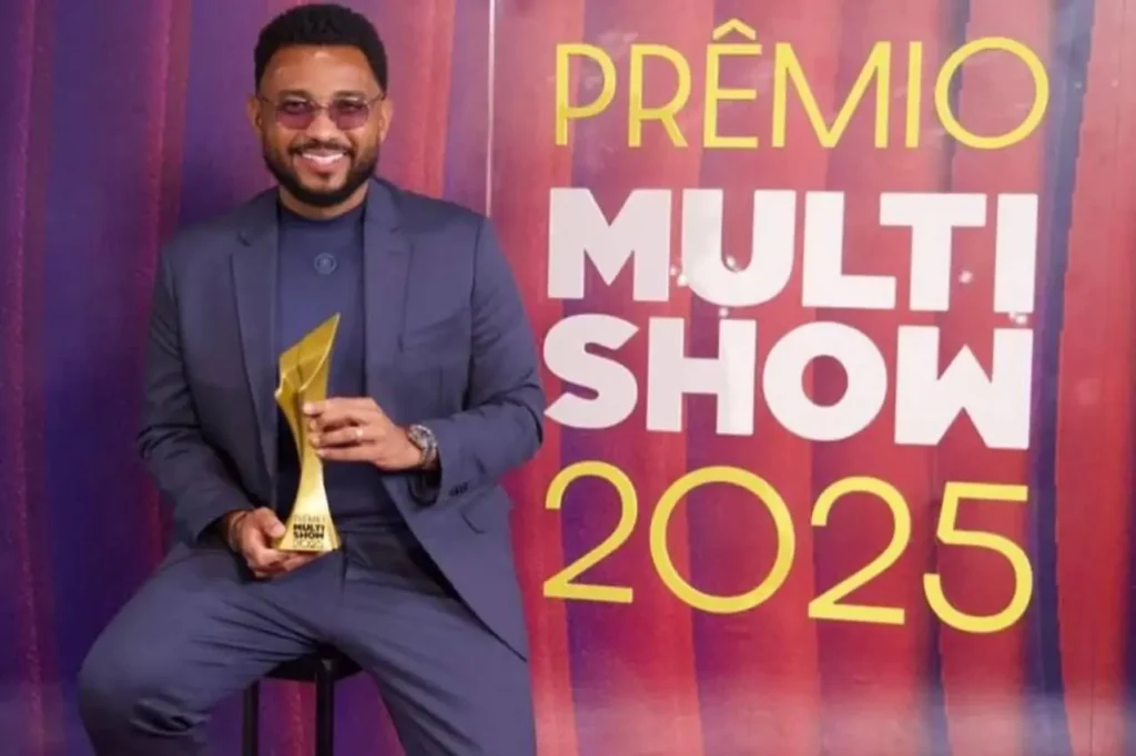Cantor segurando troféu dourado enquanto posa sorrindo diante de painel do Prêmio Multishow 2025.