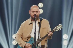 Cantor gospel se apresenta no palco tocando guitarra e cantando ao microfone durante evento cristão.