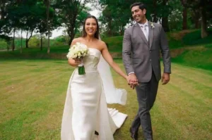 Noiva e noivo caminham de mãos dadas em área verde após cerimônia de casamento ao ar livre.