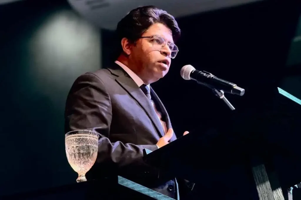 Pastor Nilson Gomes pregando com expressão séria ao microfone durante culto em igreja evangélica.