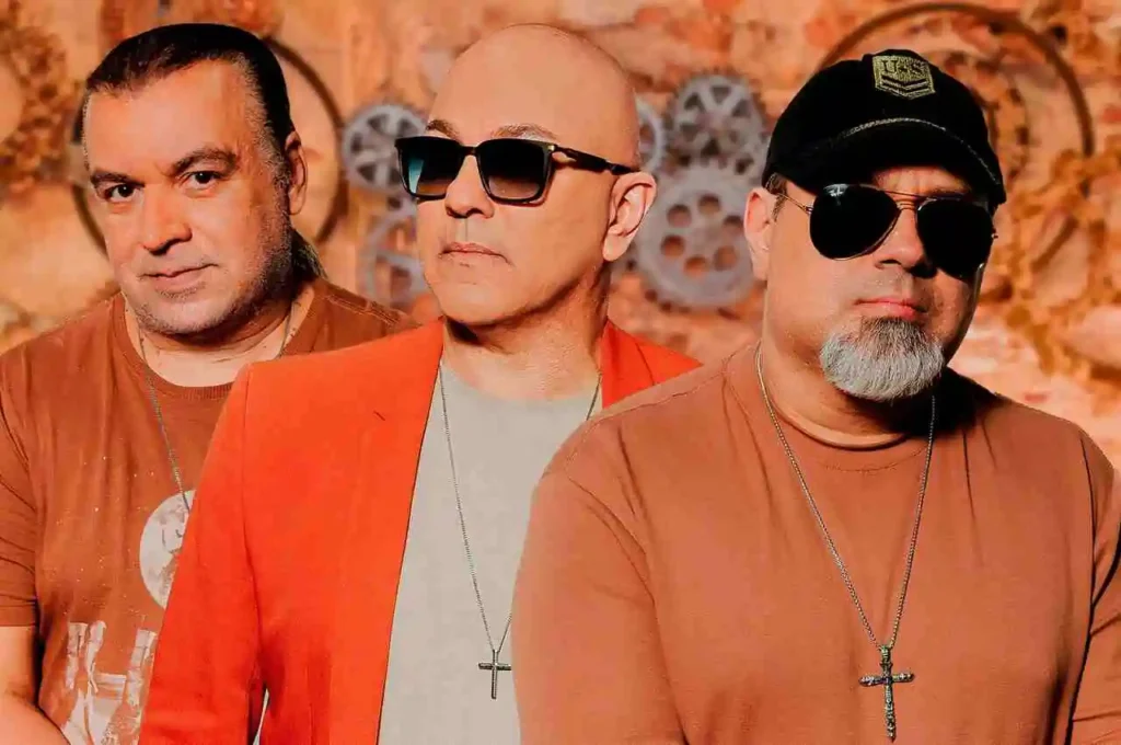 Trio musical posando para foto em estúdio, com fundo decorativo e acessórios de estilo contemporâneo.