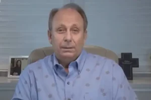 Pastor Lamartine Posella falando diretamente à câmera em ambiente interno, com cruz decorativa ao fundo.