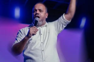 Pastor Rodrigo Gomes, líder do MEVAM Rio de Janeiro, prega ao microfone com o braço levantado durante culto