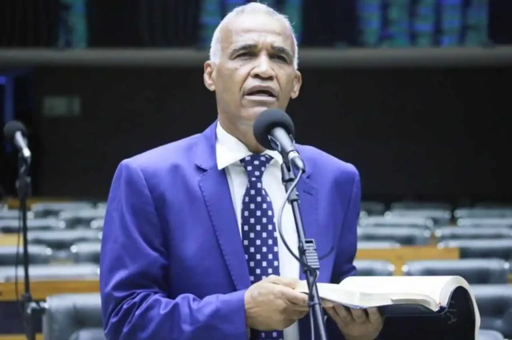 Pastor que também atua como deputado federal discursando ao microfone enquanto segura uma Bíblia no plenário.