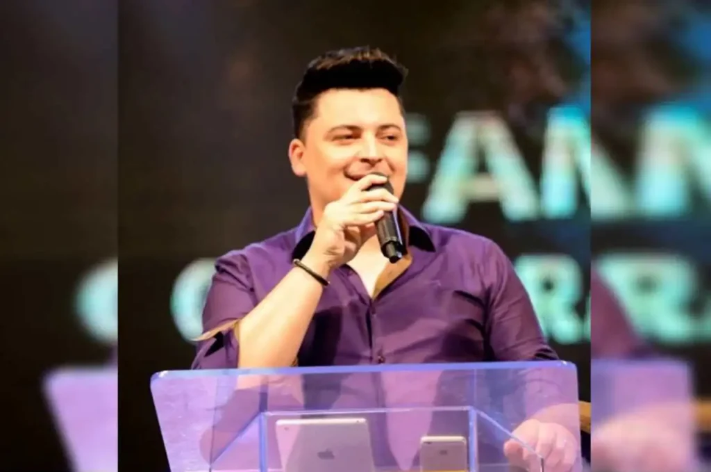 Pastor evangélico pregando ao microfone no púlpito da igreja, gesticulando com a mão durante o culto.