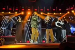 Grupo de cantores se apresentando em palco iluminado durante show gospel, com músicos e backing vocals.