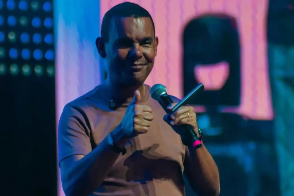 Parlamentar discursando em plenário, gesticulando com o dedo levantado enquanto fala ao microfone, com bandeira nacional ao fundo.