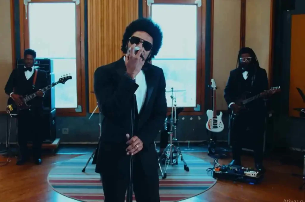 Cantor Thalles Roberto cantando de terno preto e óculos escuros durante gravação em estúdio com banda ao fundo