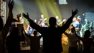 fiéis participam de culto evangélico com braços erguidos durante momento de louvor em igreja