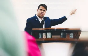 Pastor Elizeu Rodrigues prega ao microfone no púlpito e aponta para o lado durante culto