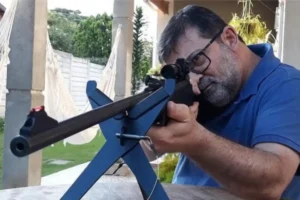 Pastor Marcos Granconato mira com arma longa apoiada em suporte em área externa, imagem usada em matéria sobre orientação a fiéis deixarem igrejas de pastores de esquerda