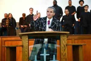 Bispo Samuel Ferreira pregando com dedo em riste no púlpito da Assembleia de Deus Ministério do Belém durante culto com coral ao fundo.