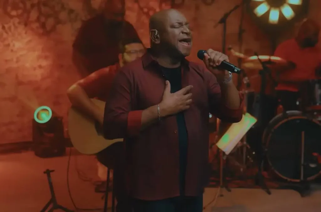 Cantor Álvaro Tito interpretando louvor com mão no peito e expressão emocionada durante gravação musical ao vivo em estúdio.