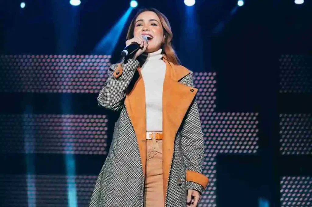 Cantora Pamela se apresenta no palco durante evento gospel, cantando com microfone.