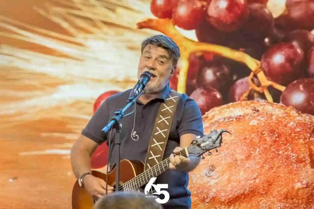 Cantor gospel Carlinhos Félix cantando e tocando violão durante apresentação cristã, com cenário temático ao fundo.
