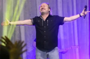 Cantor gospel David Quinlan ministra louvor com braços abertos e olhos fechados durante apresentação em culto cristão.