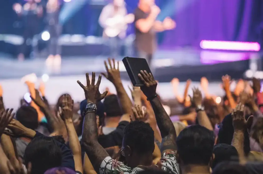 Fiéis em culto evangélico com mãos levantadas durante momento de louvor em igreja.