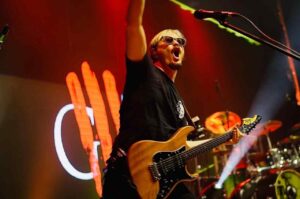 Juninho Afram, guitarrista da banda Oficina G3, tocando guitarra e interagindo com o público durante show ao vivo no palco.