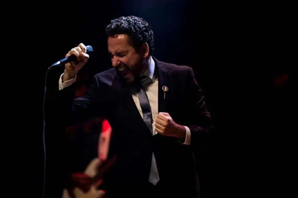 Leonardo Gonçalves canta intensamente no palco, vestindo terno escuro e gravata, segurando o microfone com expressão de emoção durante apresentação ao vivo.