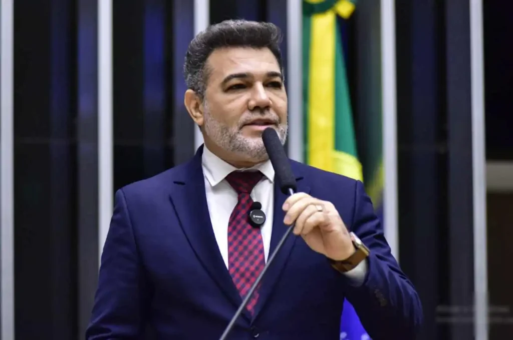 Pastor e deputado Marco Feliciano discursando ao microfone no plenário da Câmara dos Deputados, com bandeira do Brasil ao fundo.