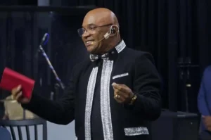 Clóvis Bernardo ministra durante culto, vestindo traje formal preto com detalhes prateados