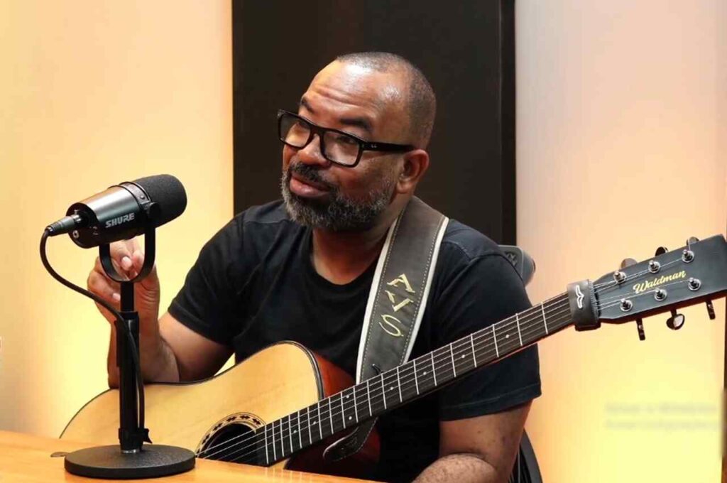 Pastor Luiz Arcanjo cantando e falando ao microfone enquanto toca violão durante gravação em estúdio.