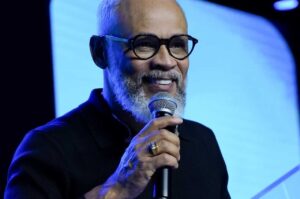 Pastor e cantor Antônio Cirilo sorrindo enquanto segura o microfone durante ministração em evento cristão com iluminação azul ao fundo.