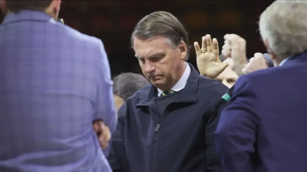 cena do documentário Apocalipse nos Trópicos mostra Jair Bolsonaro em evento público com pessoas ao redor e mãos erguidas