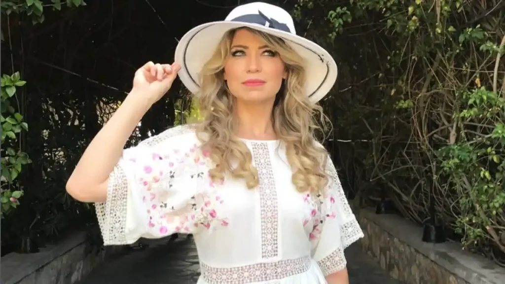 elaine de jesus posa para foto ao ar livre usando vestido branco e chapéu em ambiente natural