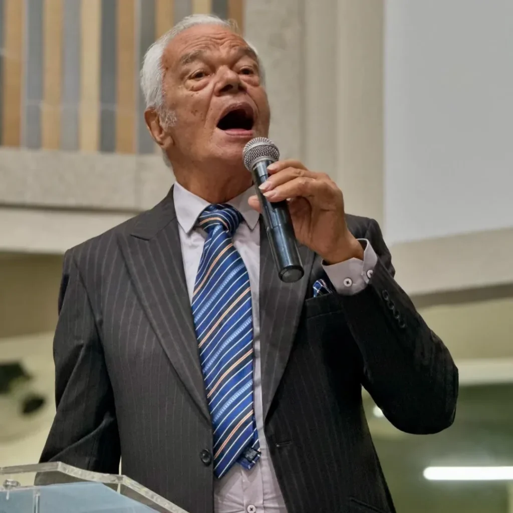 Cantor Vitorino Silva interpretando hino cristão com microfone em mão durante apresentação em igreja, com expressão intensa de louvor.