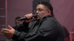 Israel Santos canta ao microfone durante apresentação em palco com iluminação rosada ao fundo