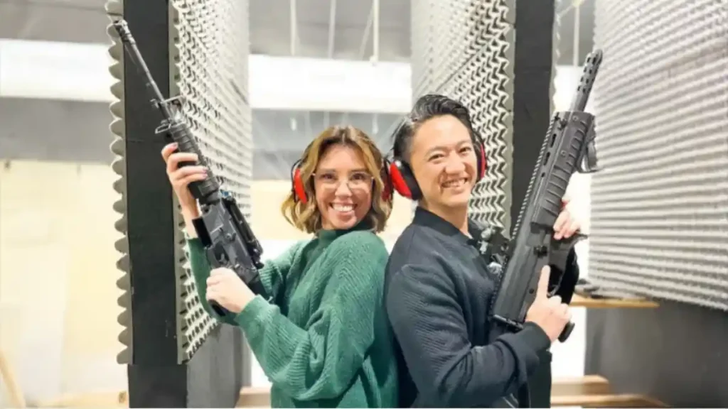 Lucas Hayashi e Jacky Hayashi posam em estande de tiro segurando armas longas e usando protetores auriculares