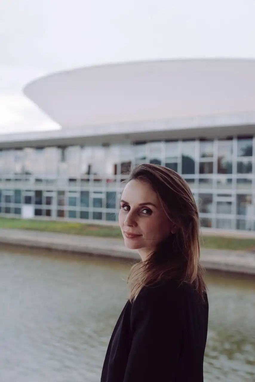 Petra Costa posa em ambiente externo com prédio ao fundo em retrato de perfil