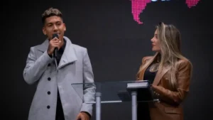 Roberto Firmino fala ao microfone ao lado da esposa durante culto na igreja Manah Church
