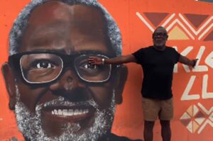 Cantor gospel Kleber Lucas posa ao lado de mural artístico com seu rosto.