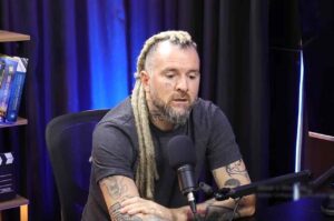 Cantor e pastor Séo Fernandes sentado em estúdio de podcast, falando ao microfone, com expressão séria e ambiente profissional ao fundo.