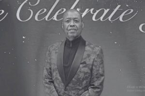 Ron Kenoly posando para foto oficial em evento, usando terno estampado, com expressão serena.