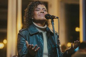 Nívea Soares cantando com os olhos fechados e mãos erguidas durante apresentação de louvor em ambiente iluminado.