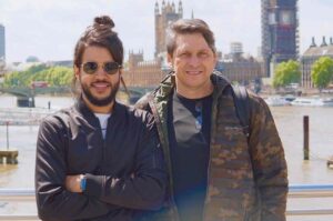 Cantor Gabriel Guedes posa ao lado do pai em área turística de Londres, com o Parlamento Britânico e o Big Ben ao fundo, em dia ensolarado.