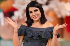 Mara Maravilha sorri para a câmera durante gravação de programa de televisão, usando vestido elegante e microfone de lapela.