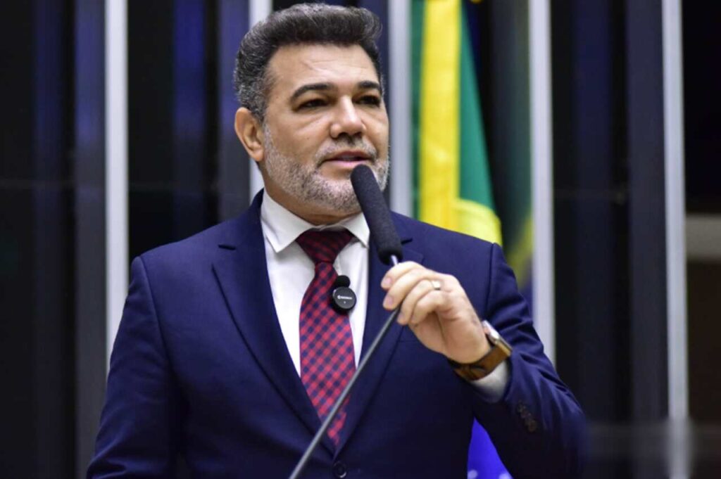 Deputado federal e pastor Marco Feliciano discursando ao microfone no plenário da Câmara dos Deputados, com bandeira do Brasil ao fundo.