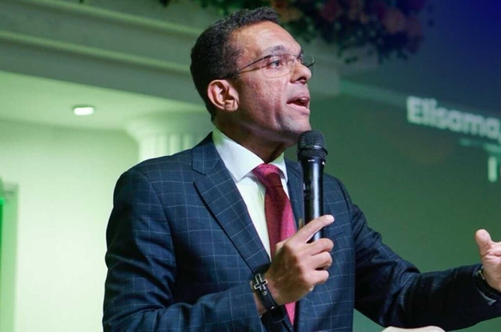 Otoni de Paula discursa em evento religioso, segurando microfone.