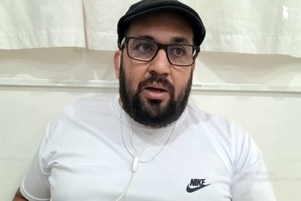 Pastor Evandro Moretti aparece em gravação de vídeo, usando camiseta branca, óculos e boné escuro, em ambiente interno