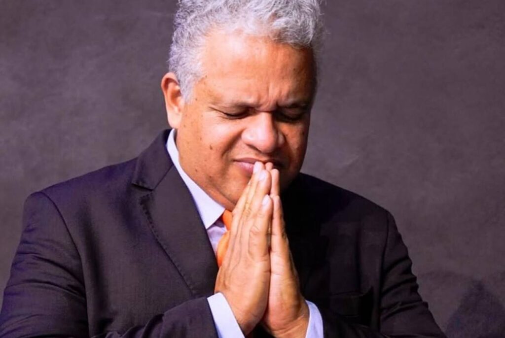 Pastor João Aguiar orando de olhos fechados com as mãos unidas em gesto de oração.