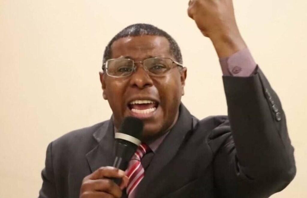 Pastor Osiel Gomes discursando com microfone na mão e braço erguido durante pregação em ambiente fechado.