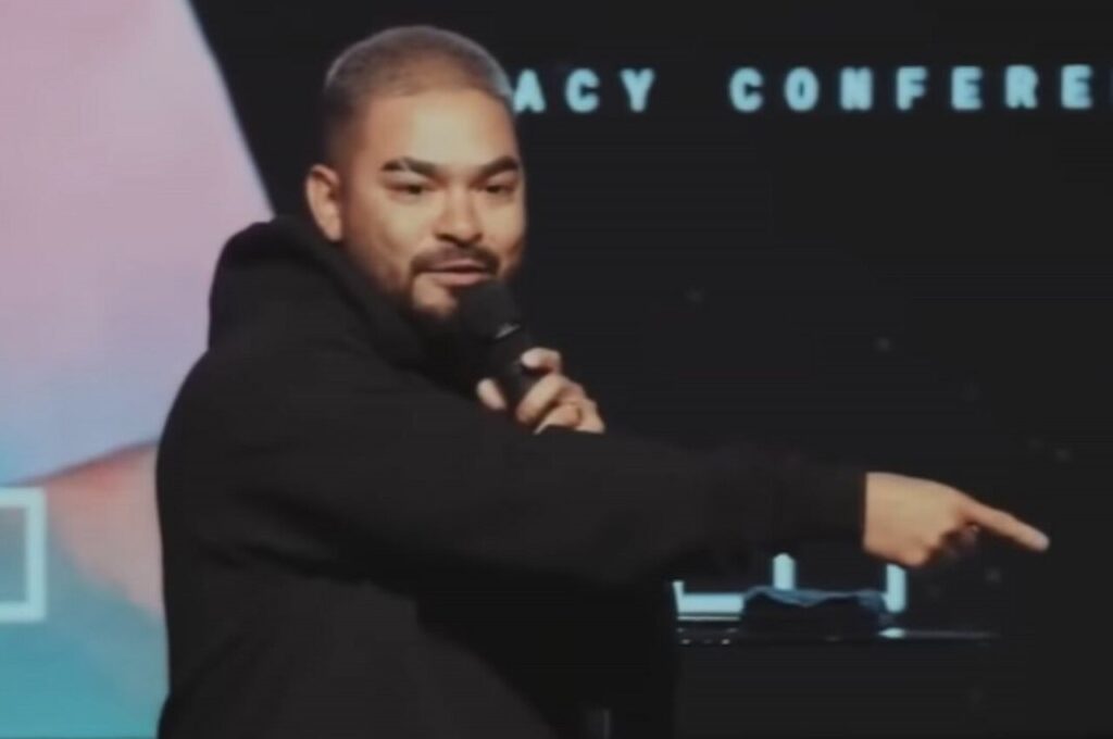 Yudi Tamashiro segura um microfone e aponta para o público durante pregação em conferência cristã.